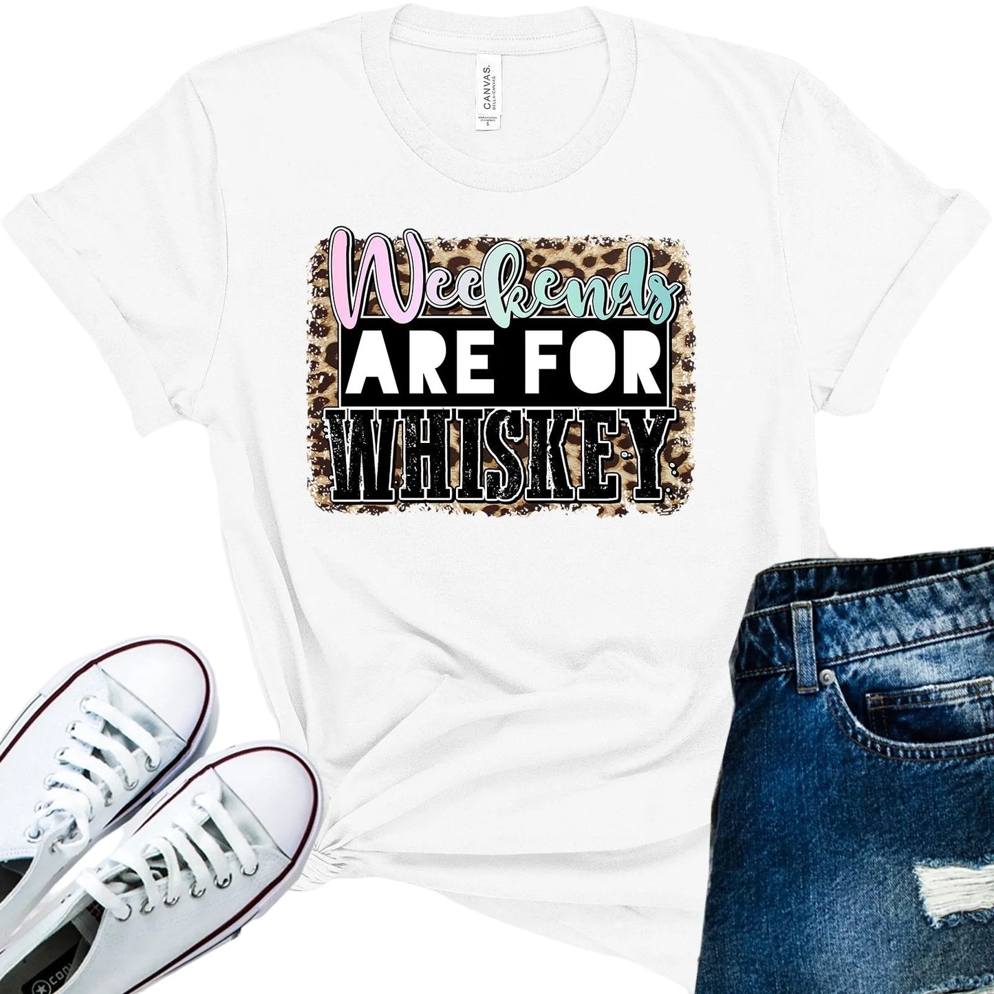 White t-shirt with 'Weekends Are For Whiskey' text on a wooden surface with white sneakers and blue jeans.