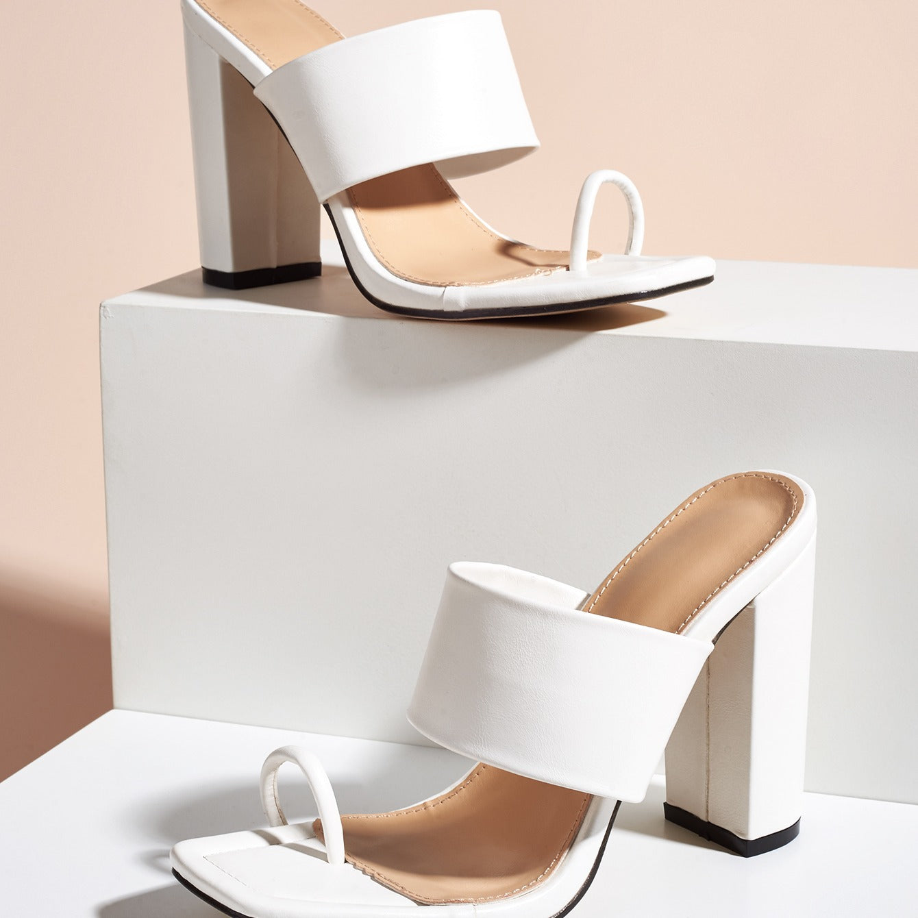 White high-heeled shoes with beige soles on a white platform against a light pink background