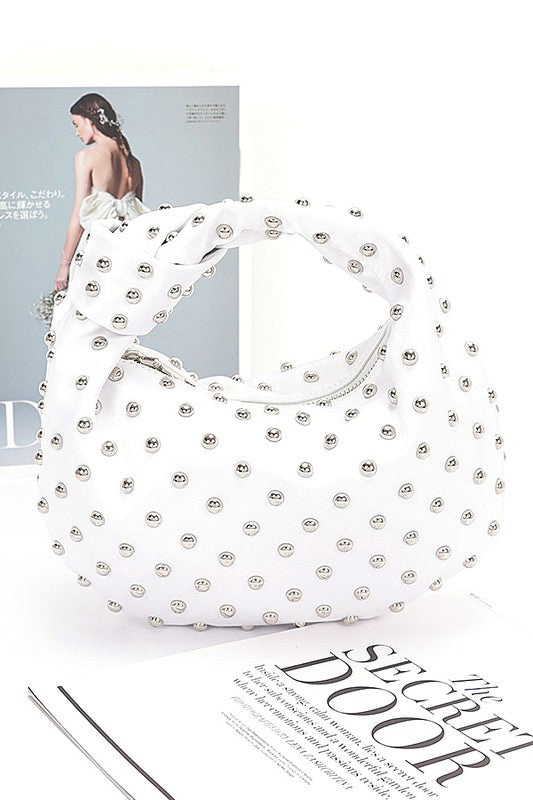 Elevate your evening look with this stunning studded clutch—the perfect blend of sophistication and sass. Featuring a chic knotted handle and soft satin construction, this compact purse slides effortlessly into your night out. The mixed metal studs add just the right amount of edge, while the polyurethane backing ensures durability. At 10" wide and 7" tall, it's sized just right for essentials. Lead and nickel compliant for worry-free style. Your new go-to accessory for turning heads.