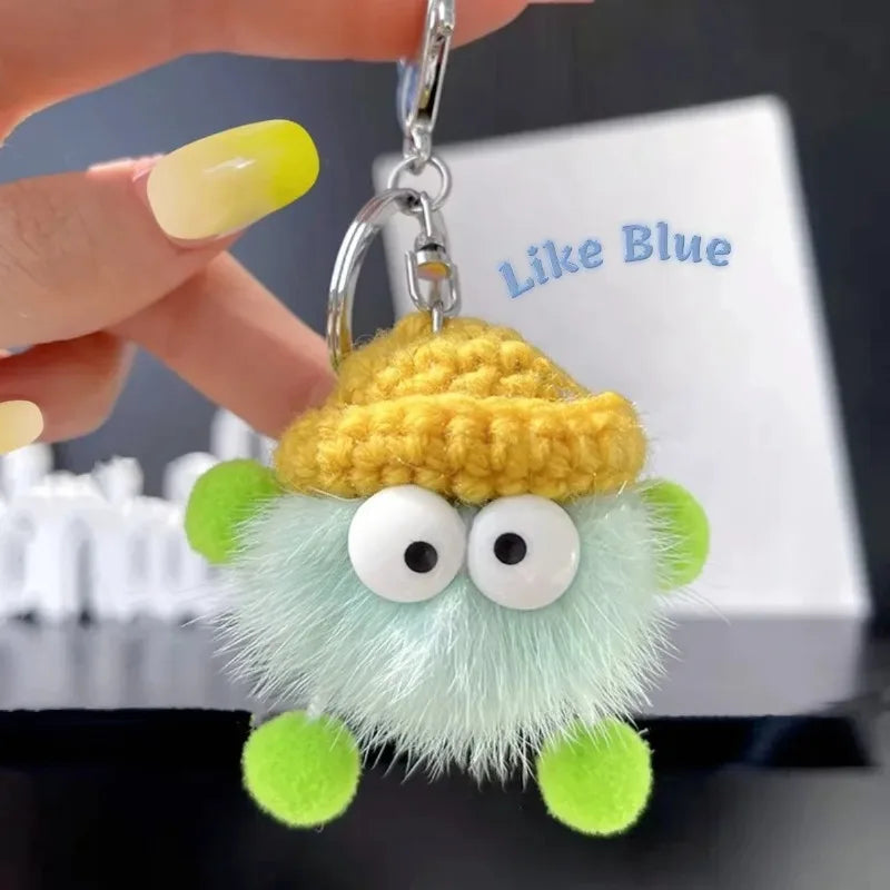 Green and yellow plush keychain held by a hand with a blurred background