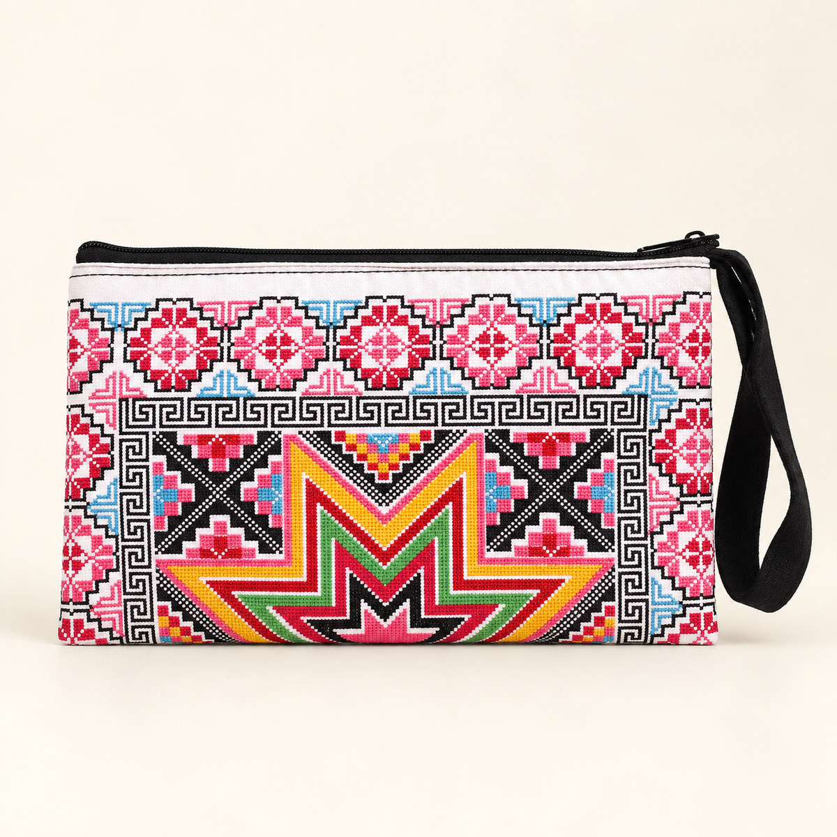 A rectangular wristlet clutch bag with a vibrant, multi-colored geometric and ethnic-inspired pattern in pink, red, yellow, green, blue, and black on a white base. It features a black zipper closure and a black wrist strap, set against a plain light beige background.
